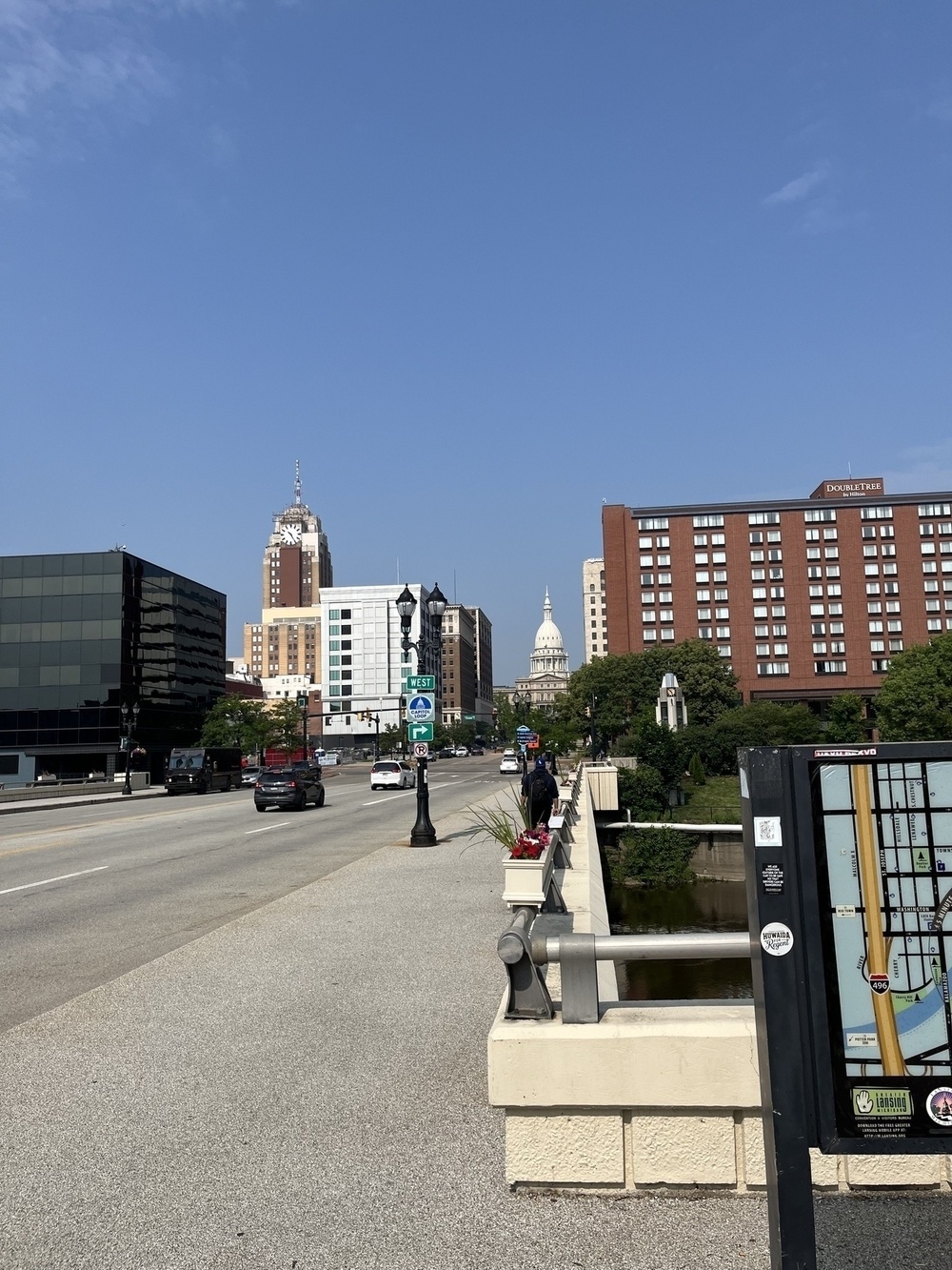 A city street scene shows a view of a distant capitol building with surrounding urban architecture under a clear blue sky.
