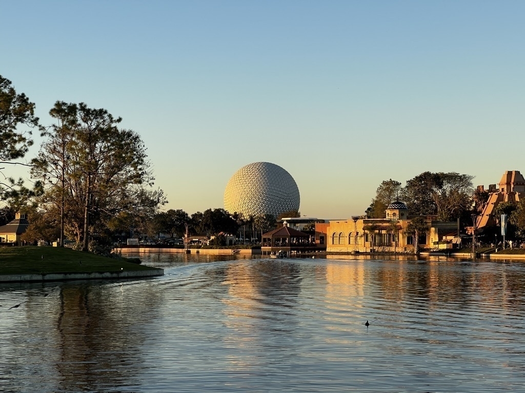 Auto-generated description: A large geodesic sphere stands prominently near a lake surrounded by trees and buildings at sunset.
