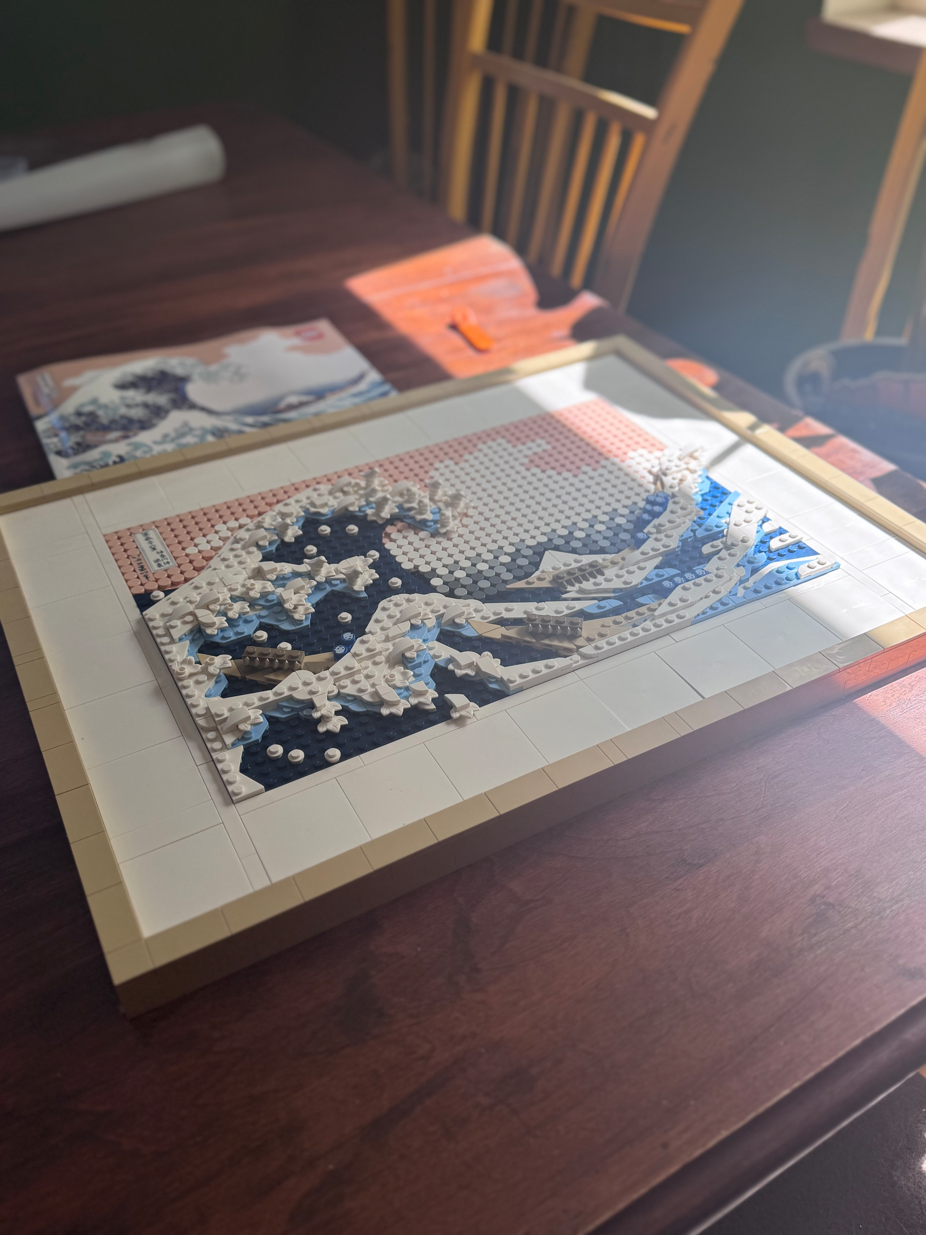 A photo of a LEGO recreation of the art print “the wave” on a kitchen table beneath the instructions booklet depicting the original art print.