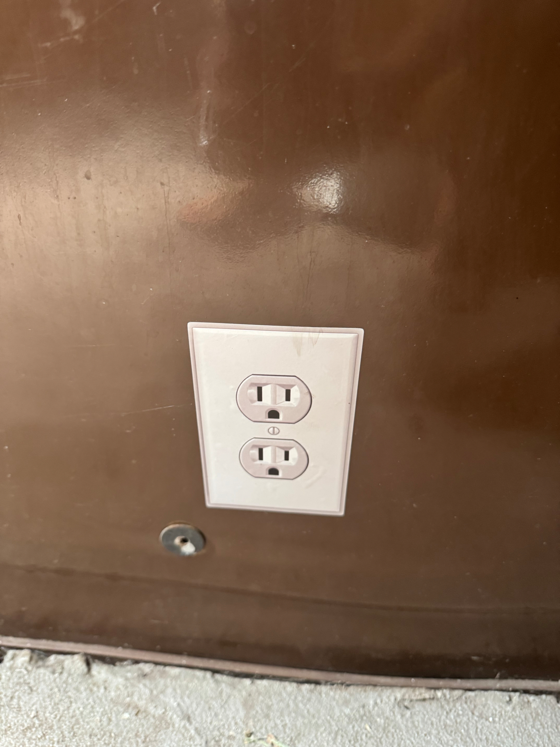 A white electrical outlet sticker on the wall of a vault toilet.