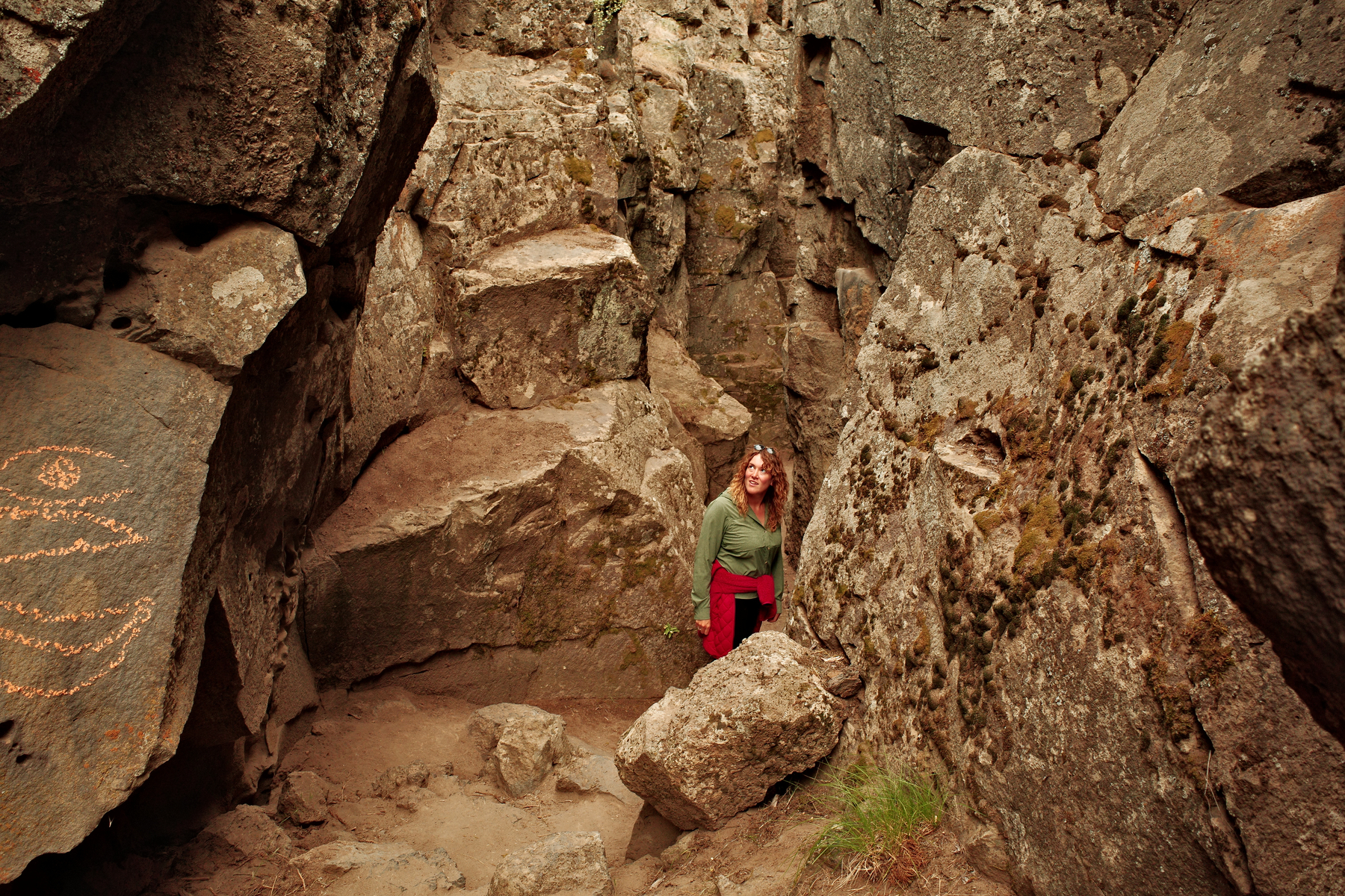 A woman surrounded by rocks, looks back towards the camera as she walks down the valley they create.
