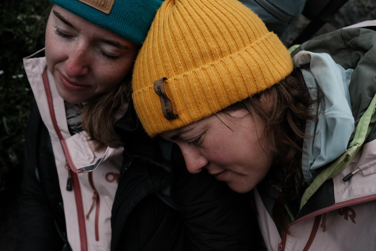 Two people wearing winter clothing and beanies are sitting closely with one resting their head on the other's shoulder. (Argentina, 2023)