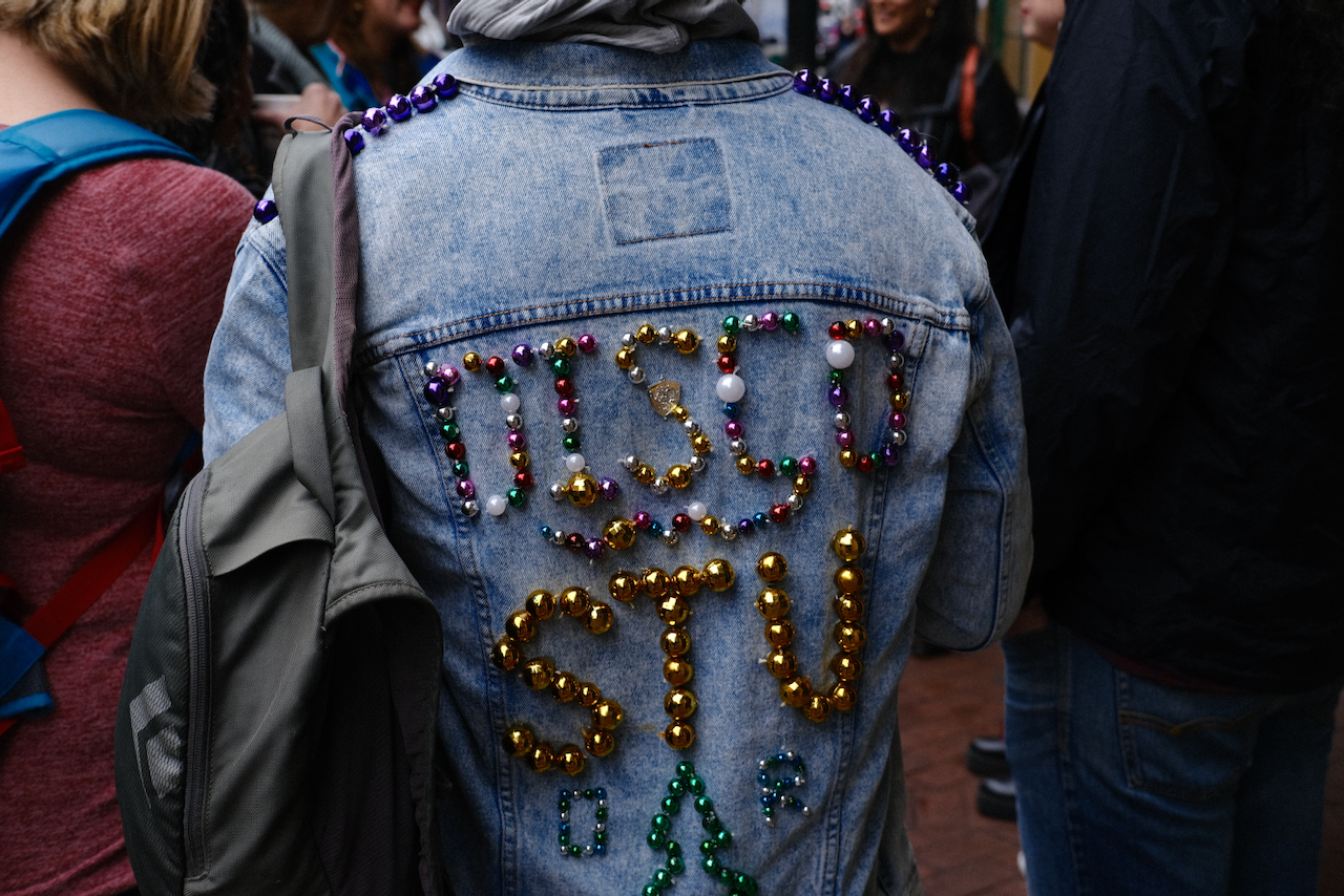 A person is wearing a denim jacket decorated with colorful beads and letters on the back. (New Orleans, 2023)