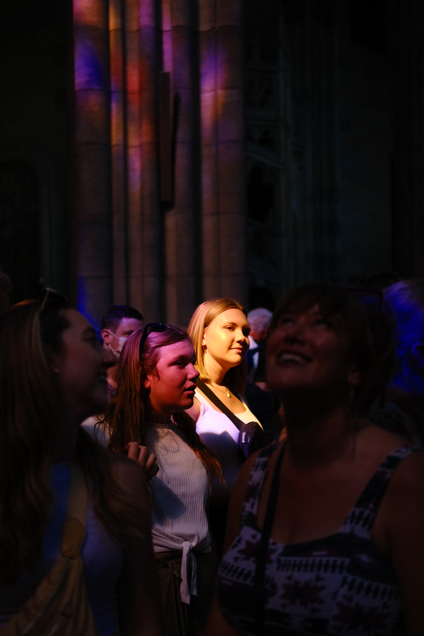 A group of people stands in a dimly lit space, illuminated by colorful lights. (Prague, 2022)