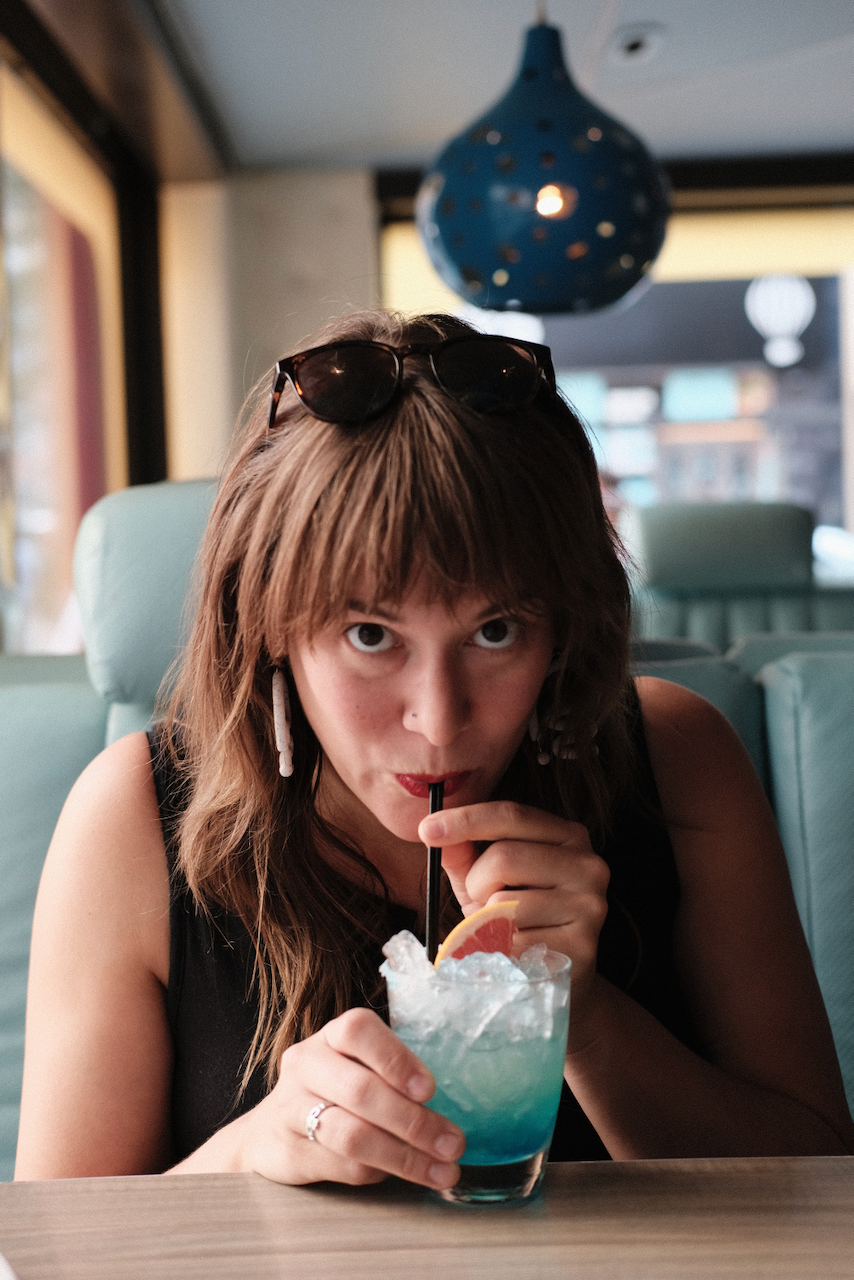A woman is sipping a blue cocktail with ice and an orange slice at a cozy café. (Philadelphia, 2021)