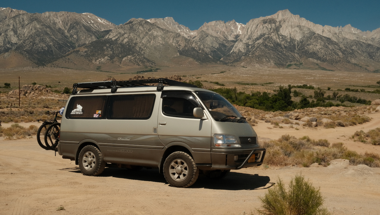 A photo of our van, Vancent, a 1998 Toyota HiAce in the desert near Bishop, California. The background shows snow dotted mountains.