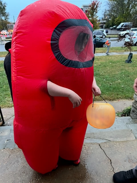 A person is wearing a red inflatable costume and holding a pumpkin-shaped container, likely for Halloween trick-or-treating.