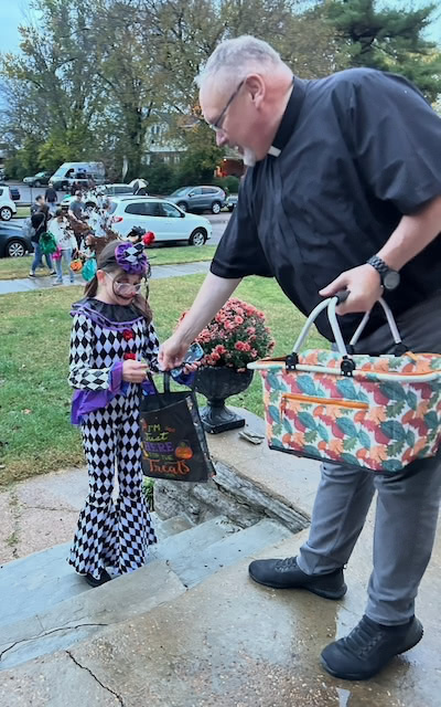 A child in a colorful costume trick-or-treats, being handed candy by a person with a basket.