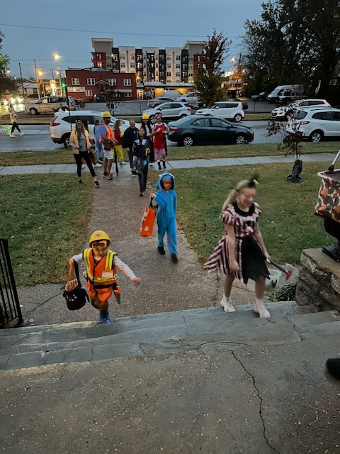 Children in various costumes are walking up a path as they go trick-or-treating.