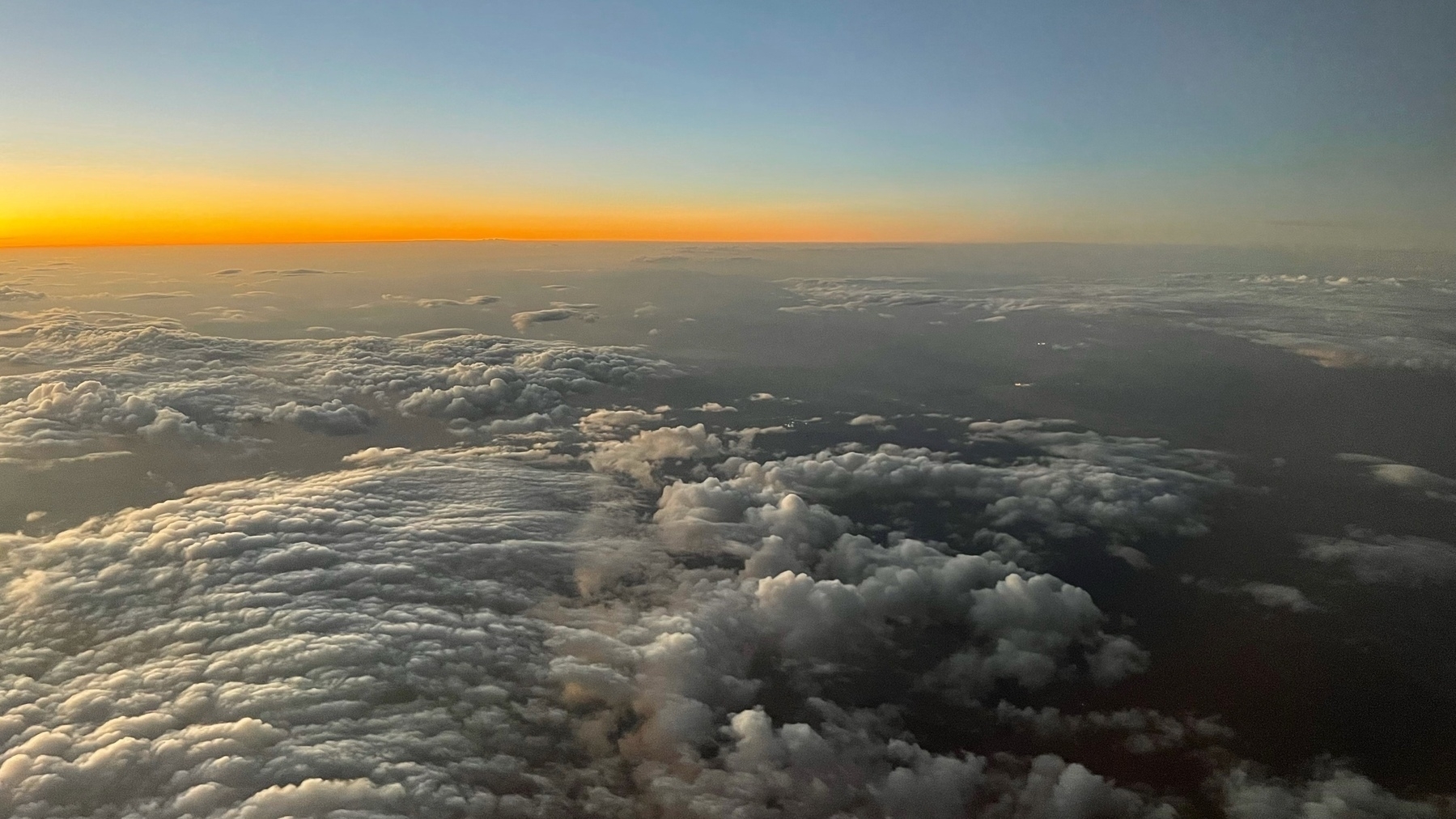 view out an aiplane window at sunset with clouds and an orange ribbon at the horizon