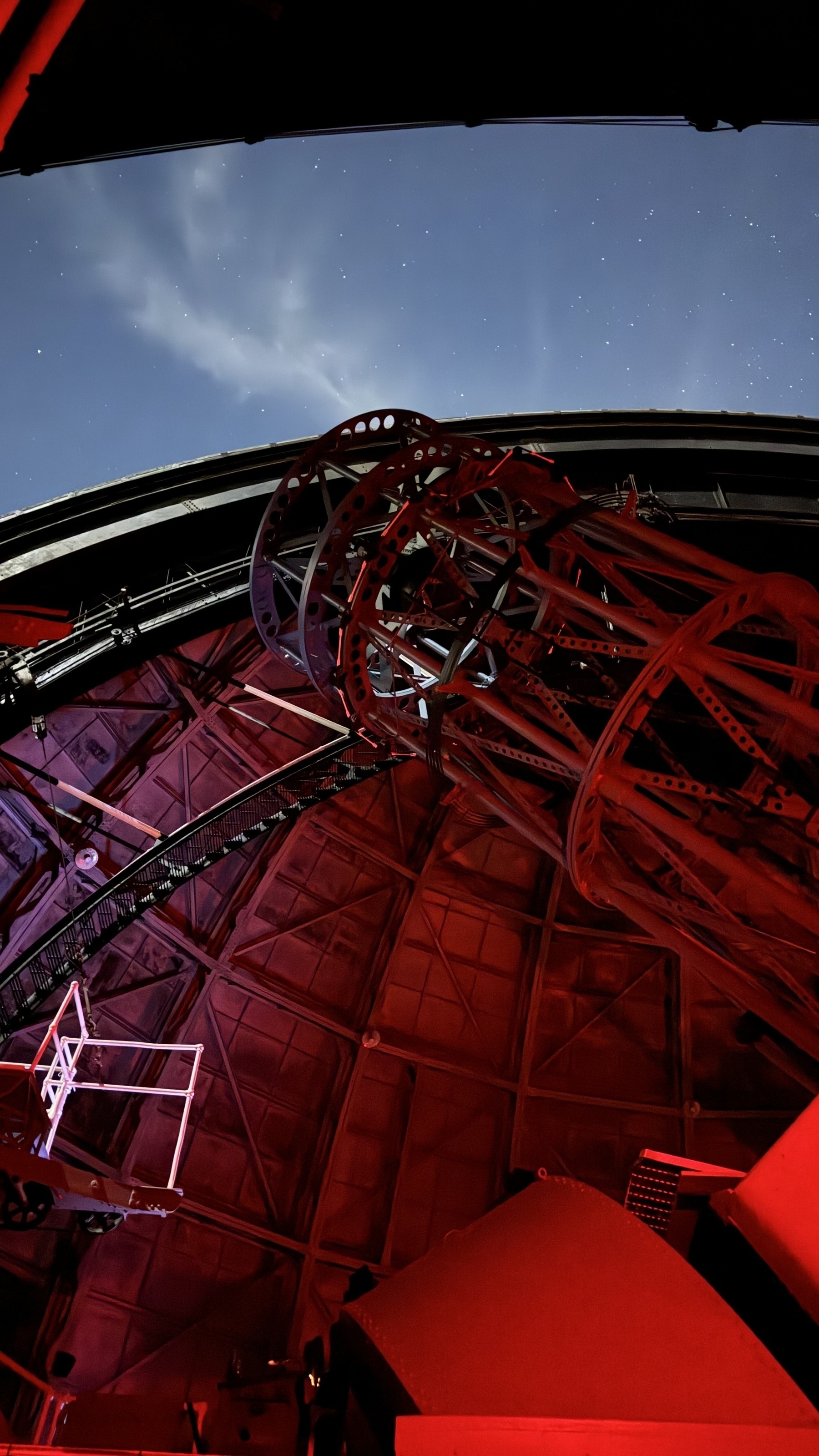 View of the 100" telescope at Mt Wilson Observatory, looking up from a red light room through the opening of the dome to the night sky and stars.