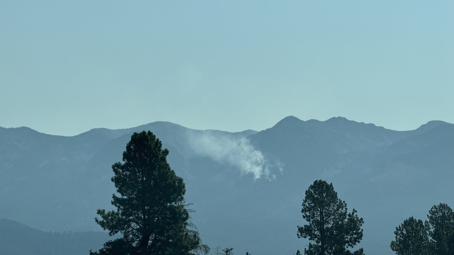 A mountain range in the mid distance with a number of smoking plumes up high on the mountain.