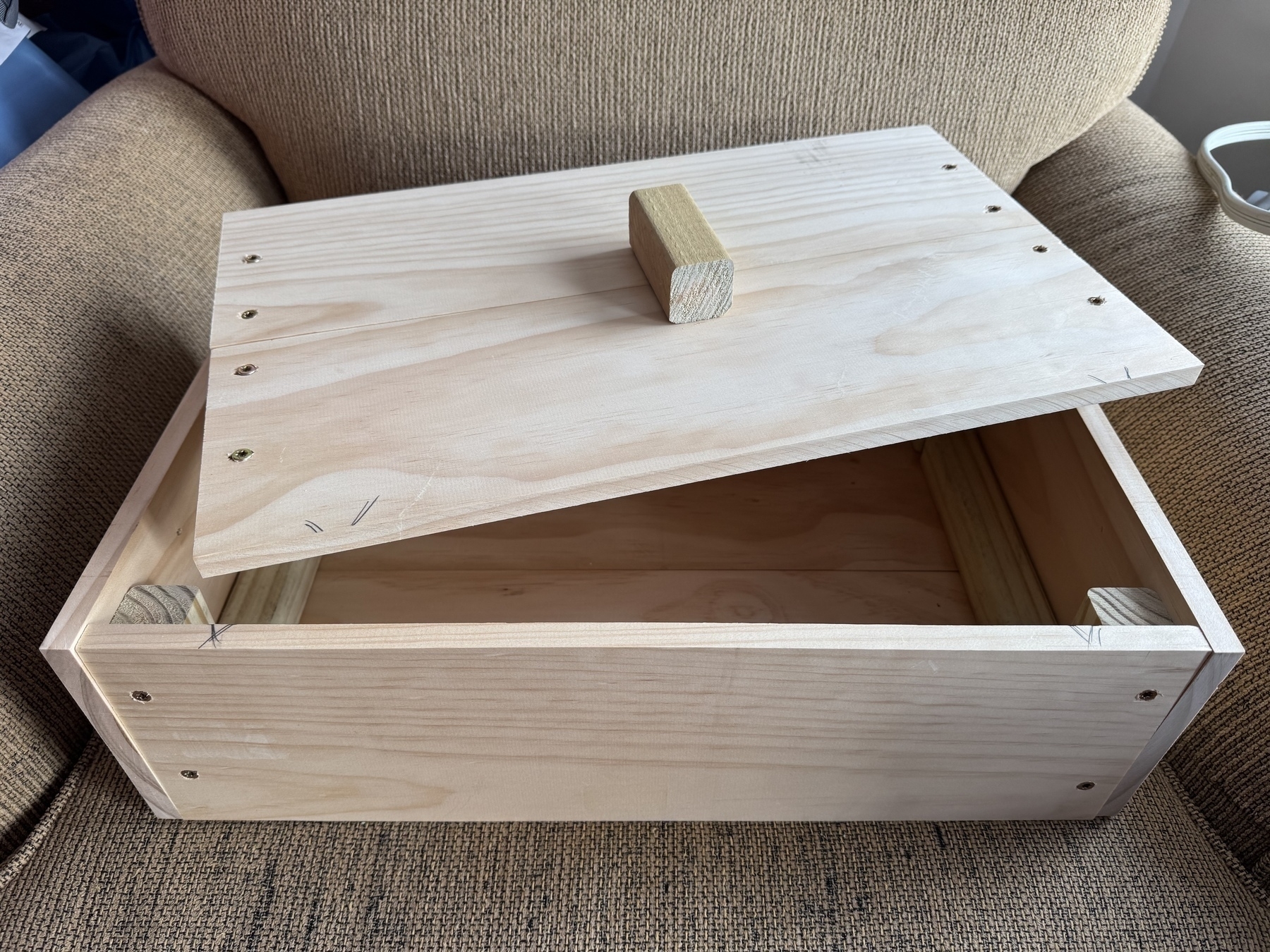 A wooden box with a partially open lid and a square handle is resting on a textured surface.