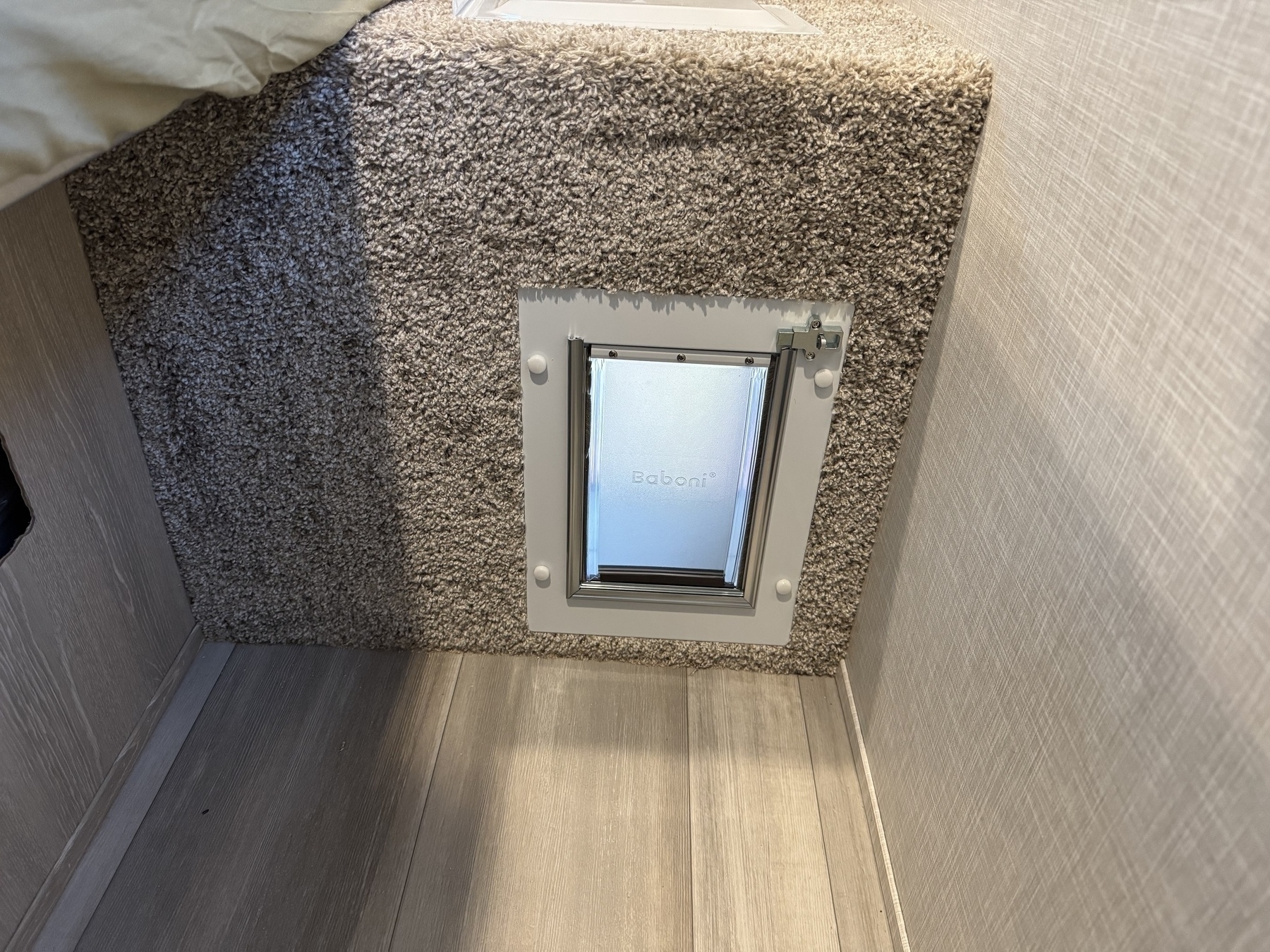 A pet door is installed within a carpeted wall area next to a wooden floor.