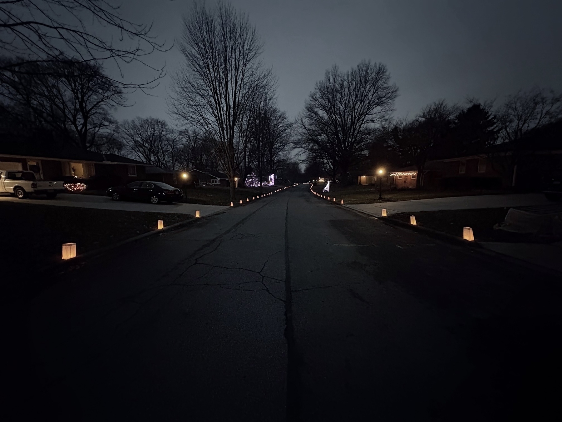 Auto-generated description: A dimly lit suburban street at night is lined with glowing lanterns and framed by leafless trees and houses.