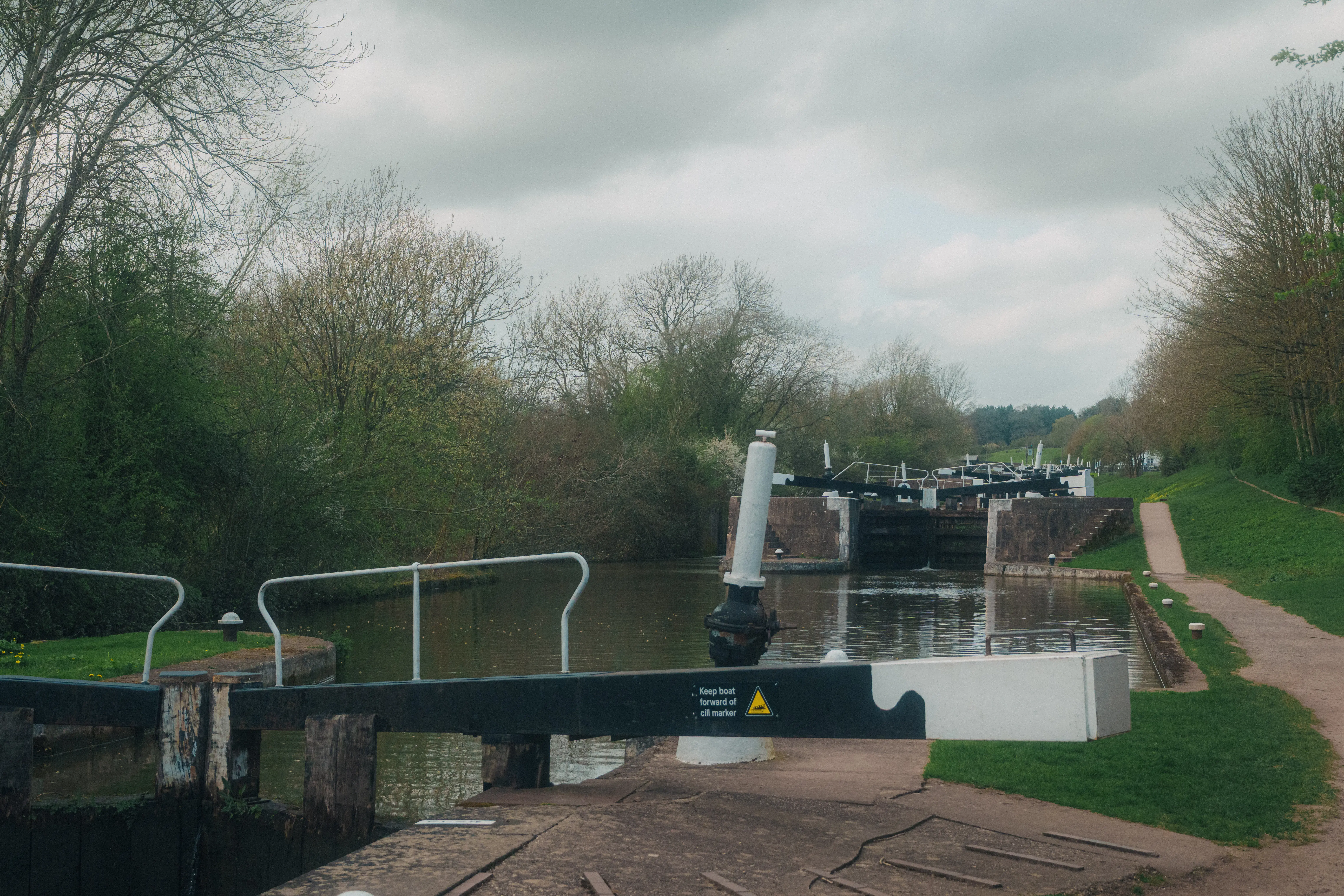 A canal lock system is visible alongside a path lined with trees under a cloudy sky.