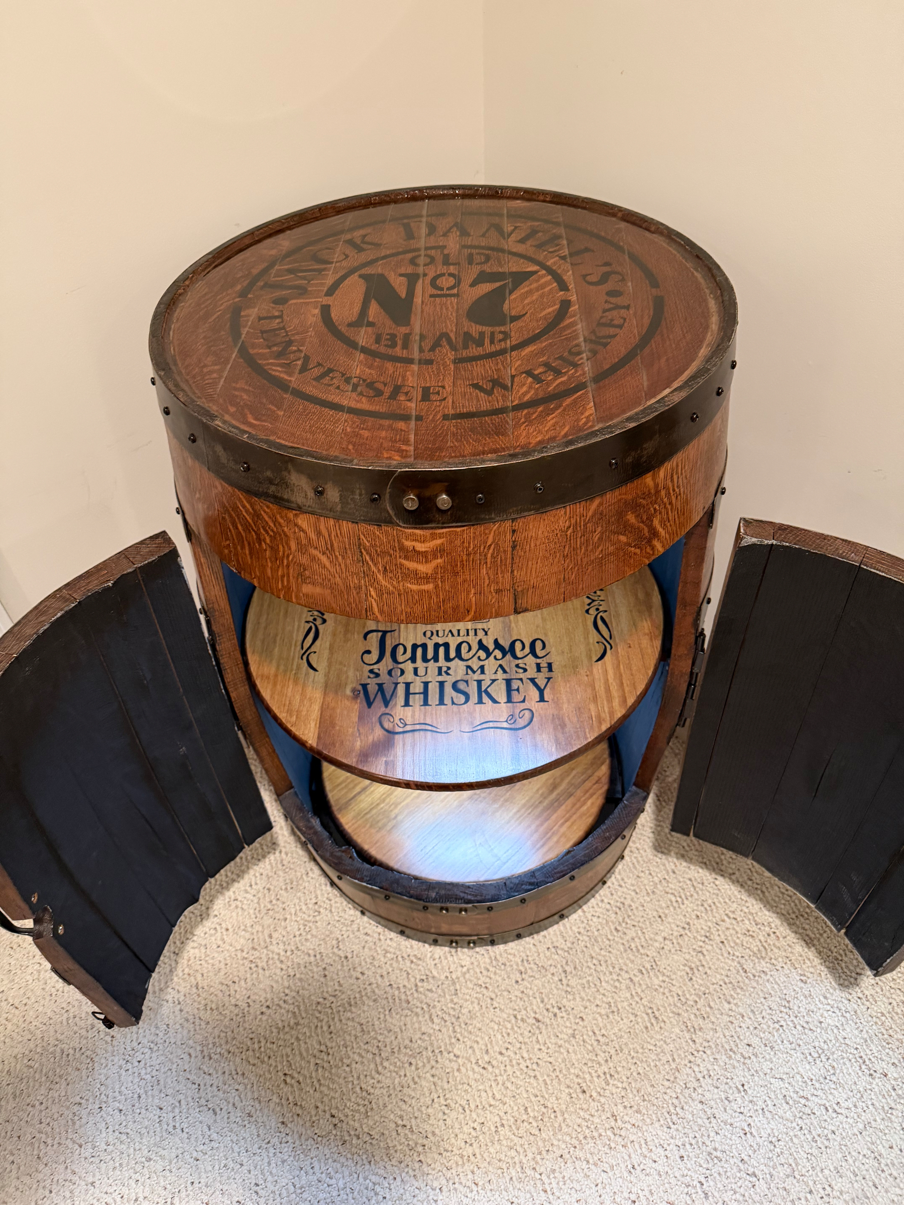 A wooden barrel designed as a custom cabinet with open doors revealing a circular shelf labeled Quality Tennessee Sour Mash Whiskey.