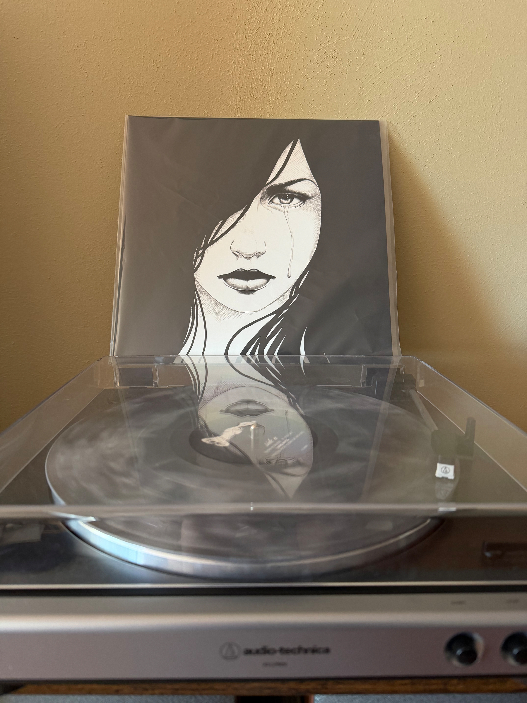 A vinyl record is playing on a turntable, with an album cover featuring an illustrated woman's face positioned behind it. Album is Desth is Silent by Kno