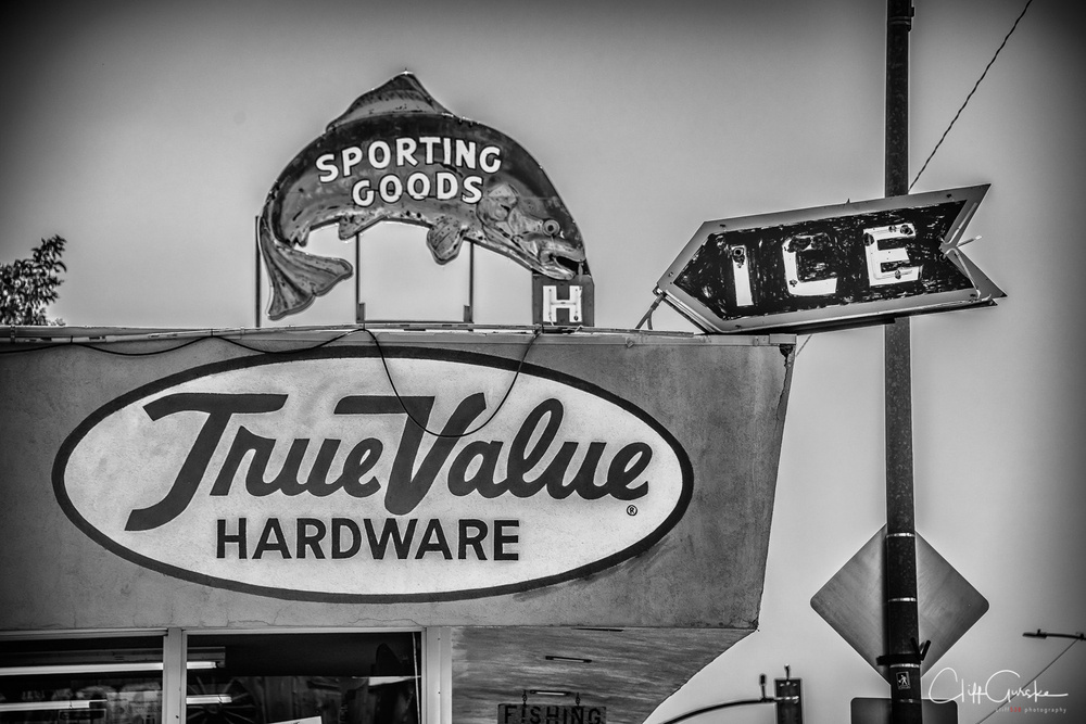 A vintage-style sign for True Value Hardware features a fish-shaped Sporting Goods sign and an arrow-shaped Ice sign.