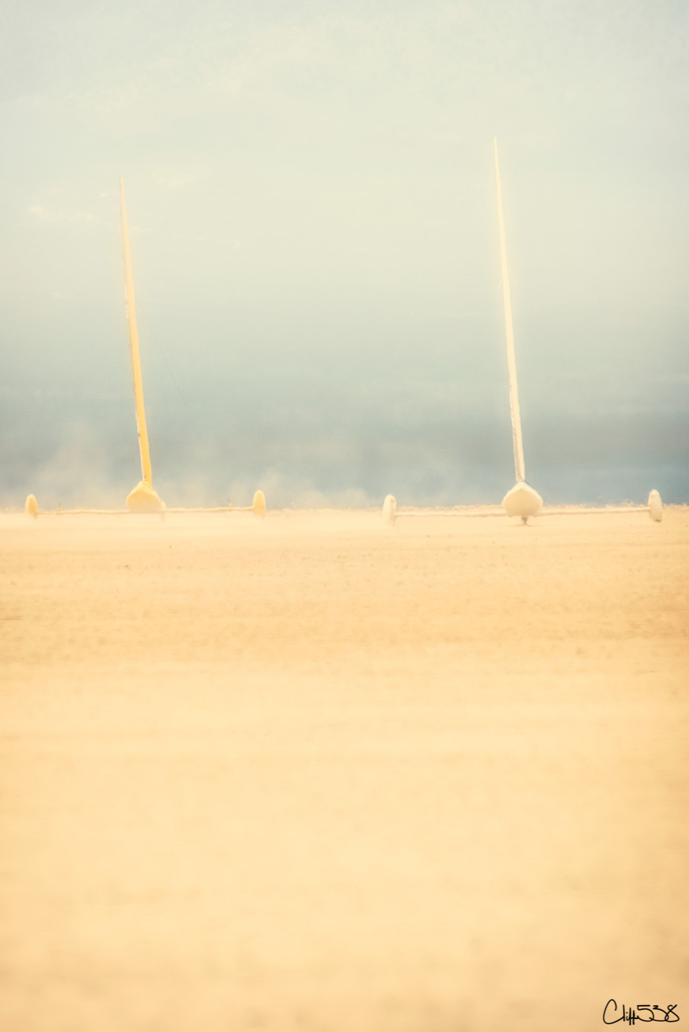 Abstract vertical objects in a hazy, somewhat desolate landscape with a signature at the bottom right.