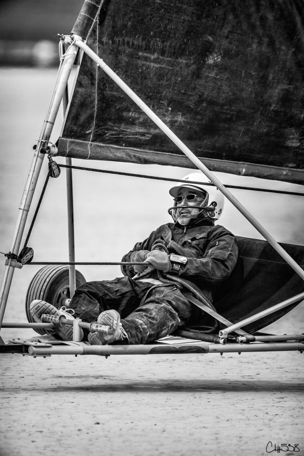 A person is riding a land sailing vehicle on a sandy surface, wearing goggles and protective clothing.