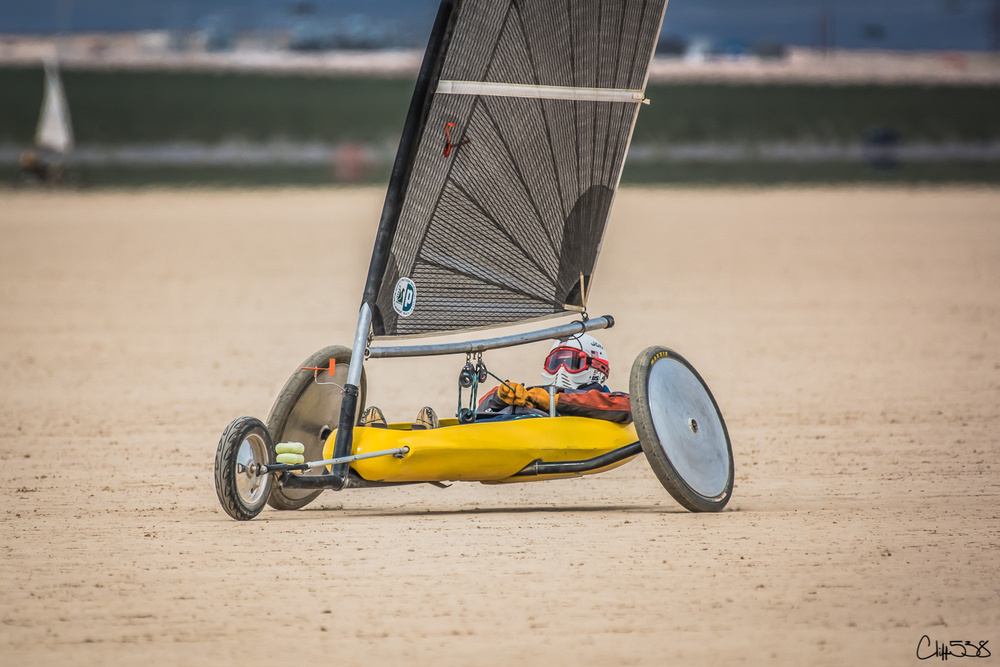 A person is navigating a land yacht with a large sail on a sandy surface.