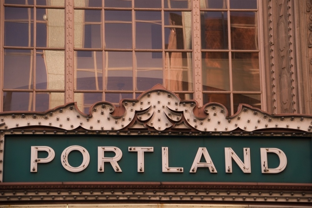 A vintage-style sign with the word Portland is displayed in front of a building with decorative elements and large windows.