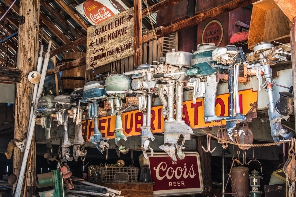 An assortment of vintage outboard motors hangs from the ceiling of a rustic building filled with old signs and eclectic memorabilia.