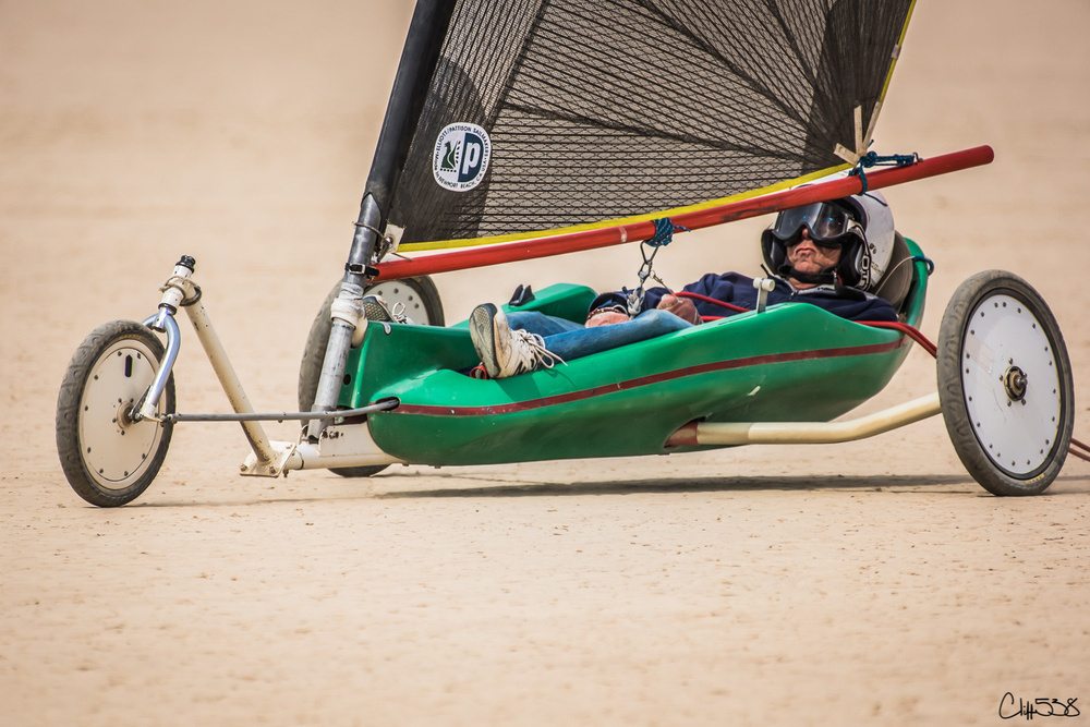 A person is riding a land sailing vehicle on a sandy surface.