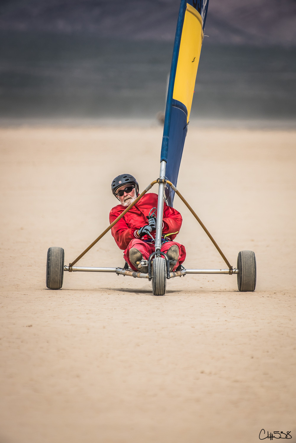 A person is joyfully riding a land sailboat on a vast, sandy surface.