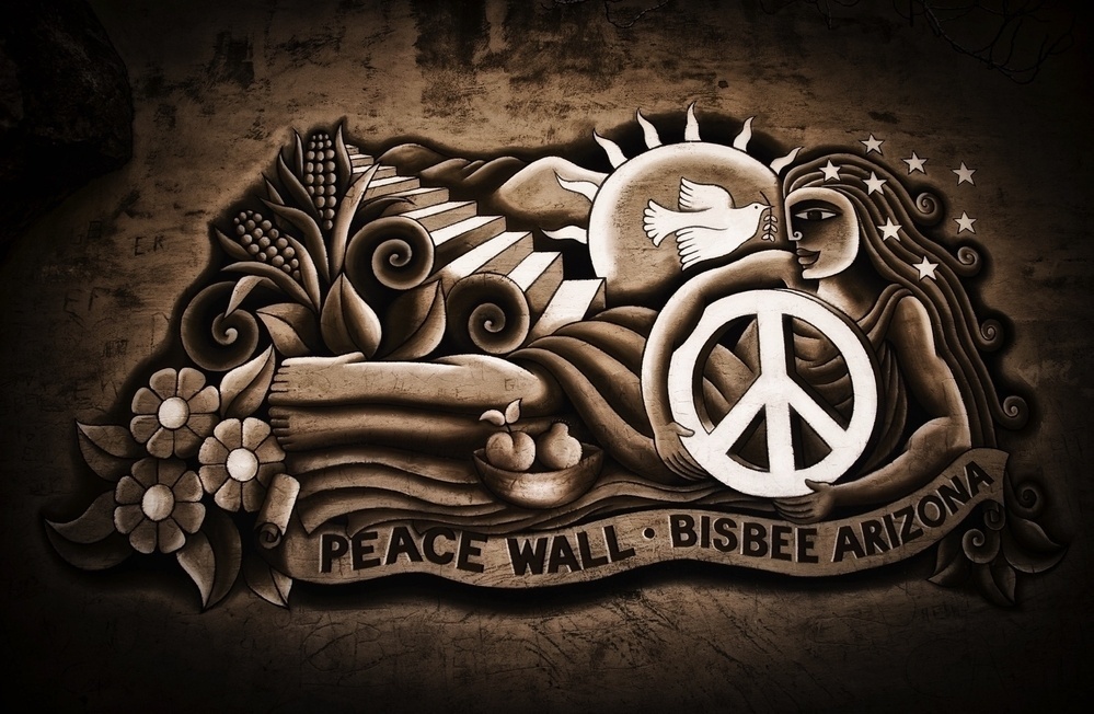 A mural depicts symbols of peace, nature, and harmony, with the words Peace Wall - Bisbee Arizona included.