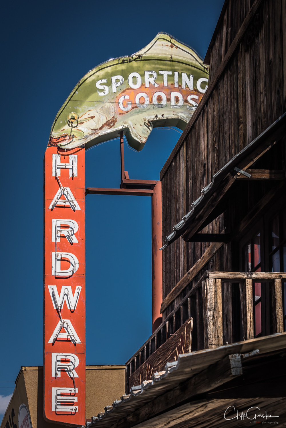 An old, vintage sign for sporting goods and hardware is mounted on a rustic wooden building.