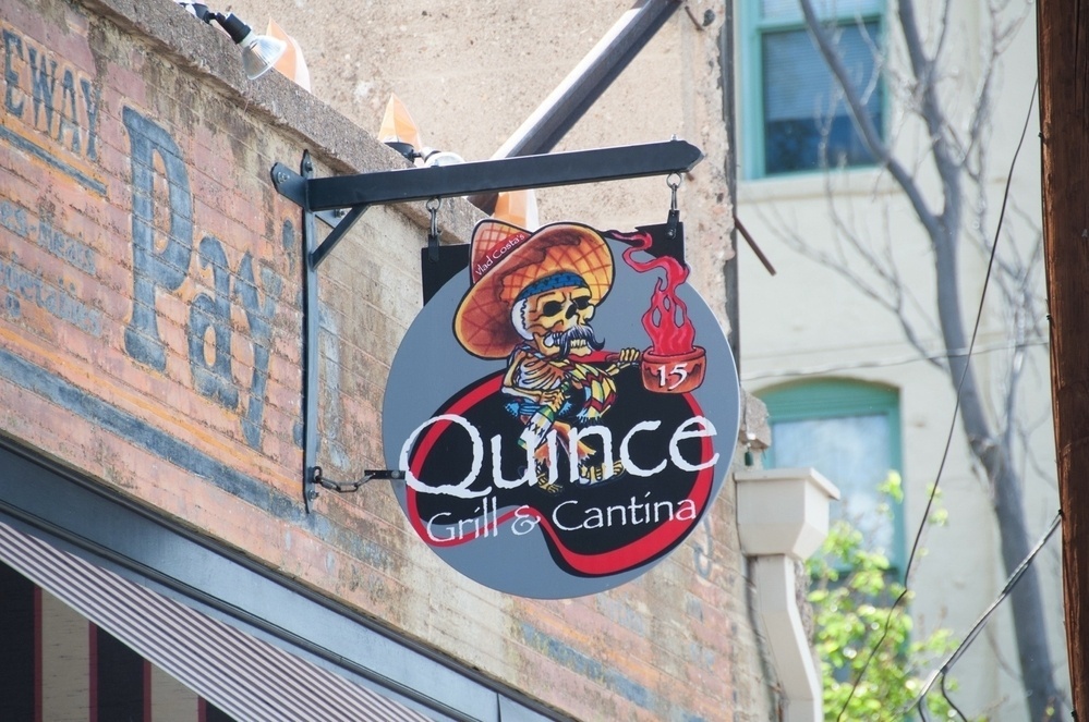 A sign for Quince Grill & Cantina features a skeleton wearing a sombrero.