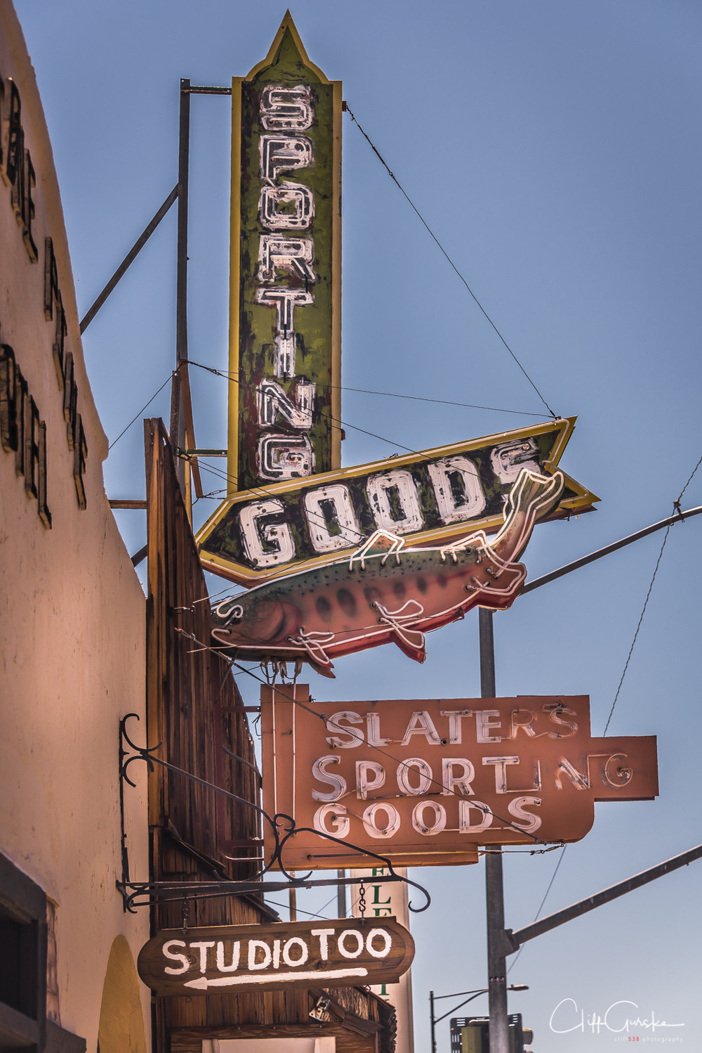 An array of vintage storefront signs includes Slater's Sporting Goods and Studio Too against a clear sky.