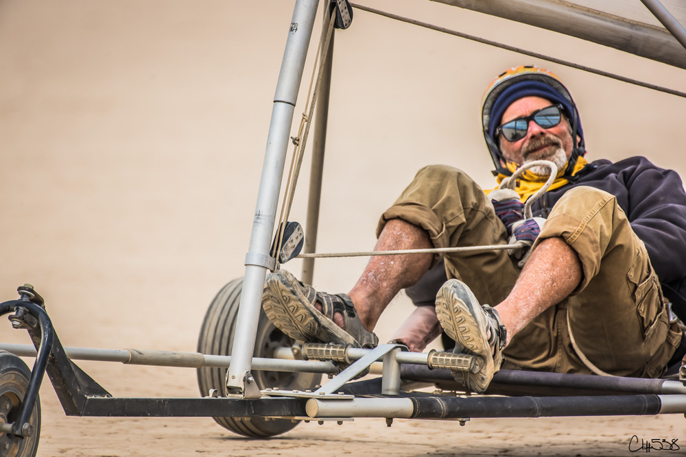 A person is happily riding a land sail vehicle on a sandy surface.