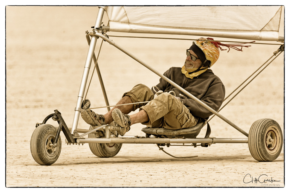 A person is seated in a metal-framed land sailing vehicle on a sandy surface.