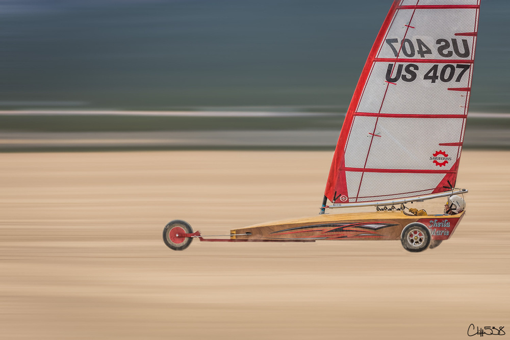 A land yacht with a red sail labeled US 407 races swiftly across a sandy surface.