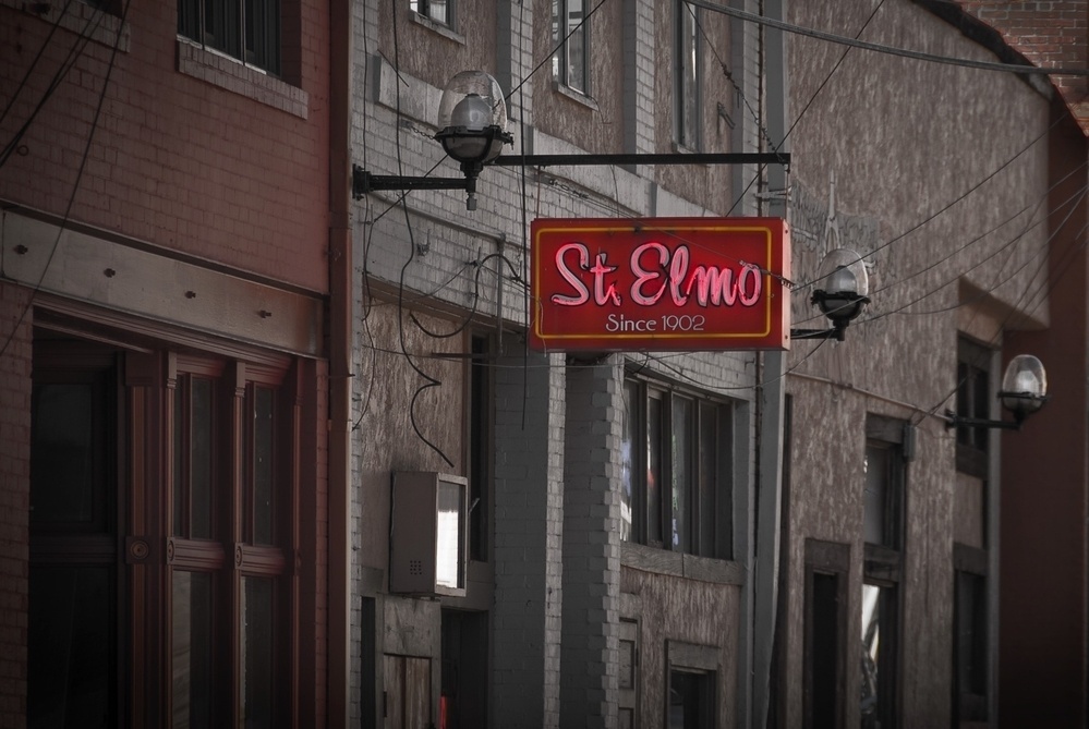 A street view showcases a hanging sign for St Elmo with the tagline Since 1902 on a row of urban buildings.