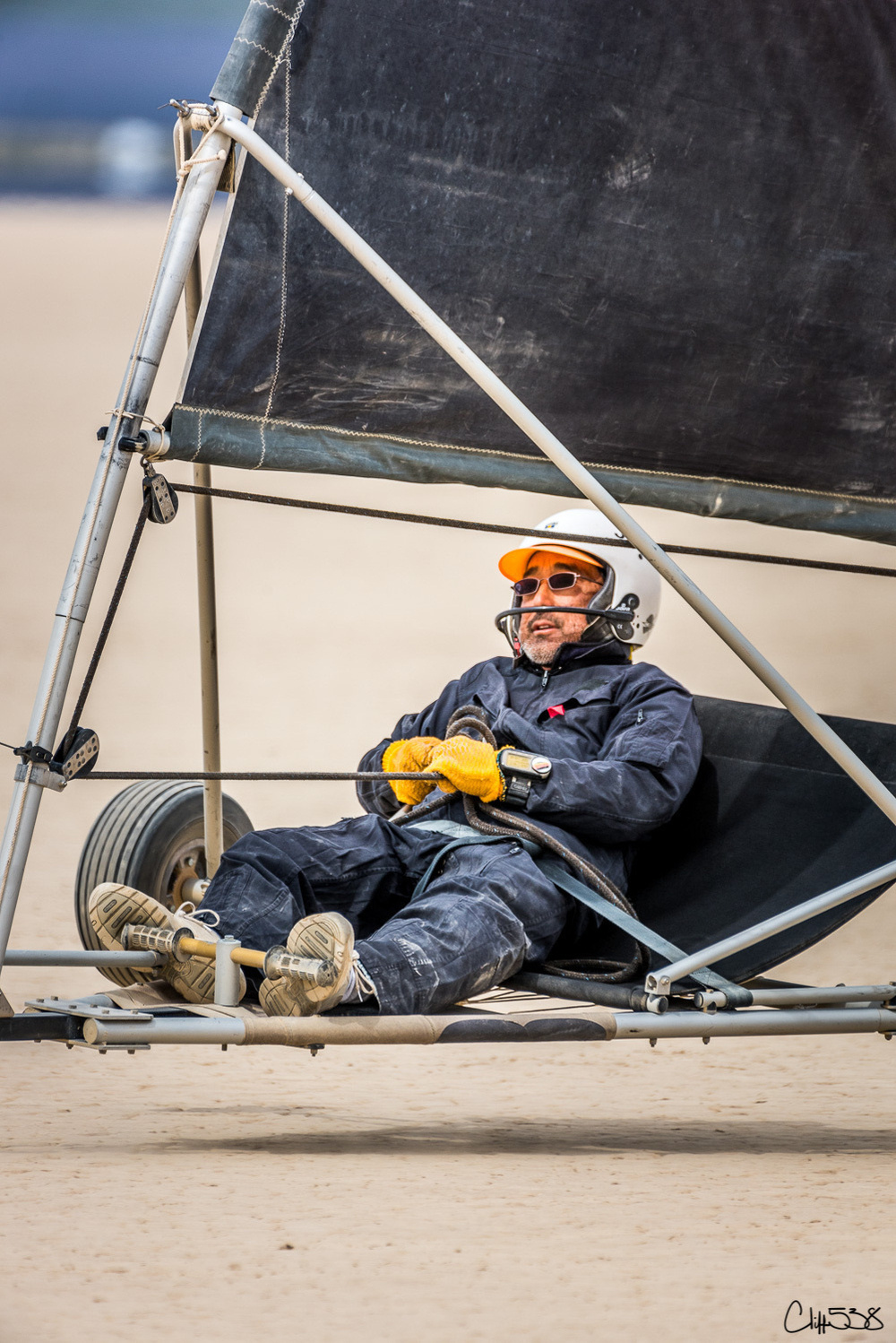 A person wearing protective gear is joyfully piloting a land yacht on a sandy surface.