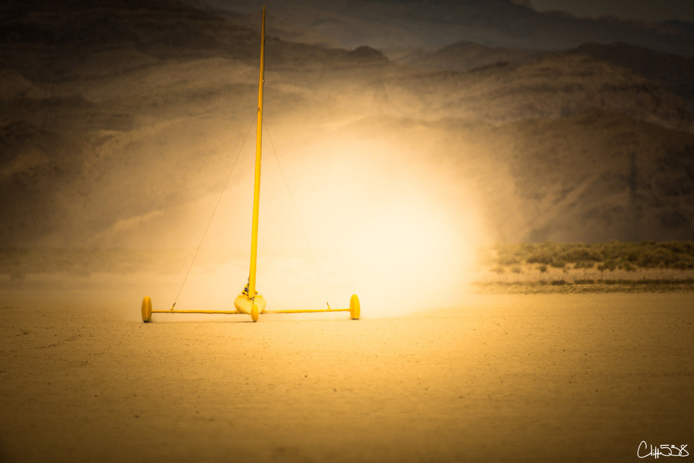 A land yacht is speeding across a desert landscape, creating a dramatic cloud of dust under warm, golden light.