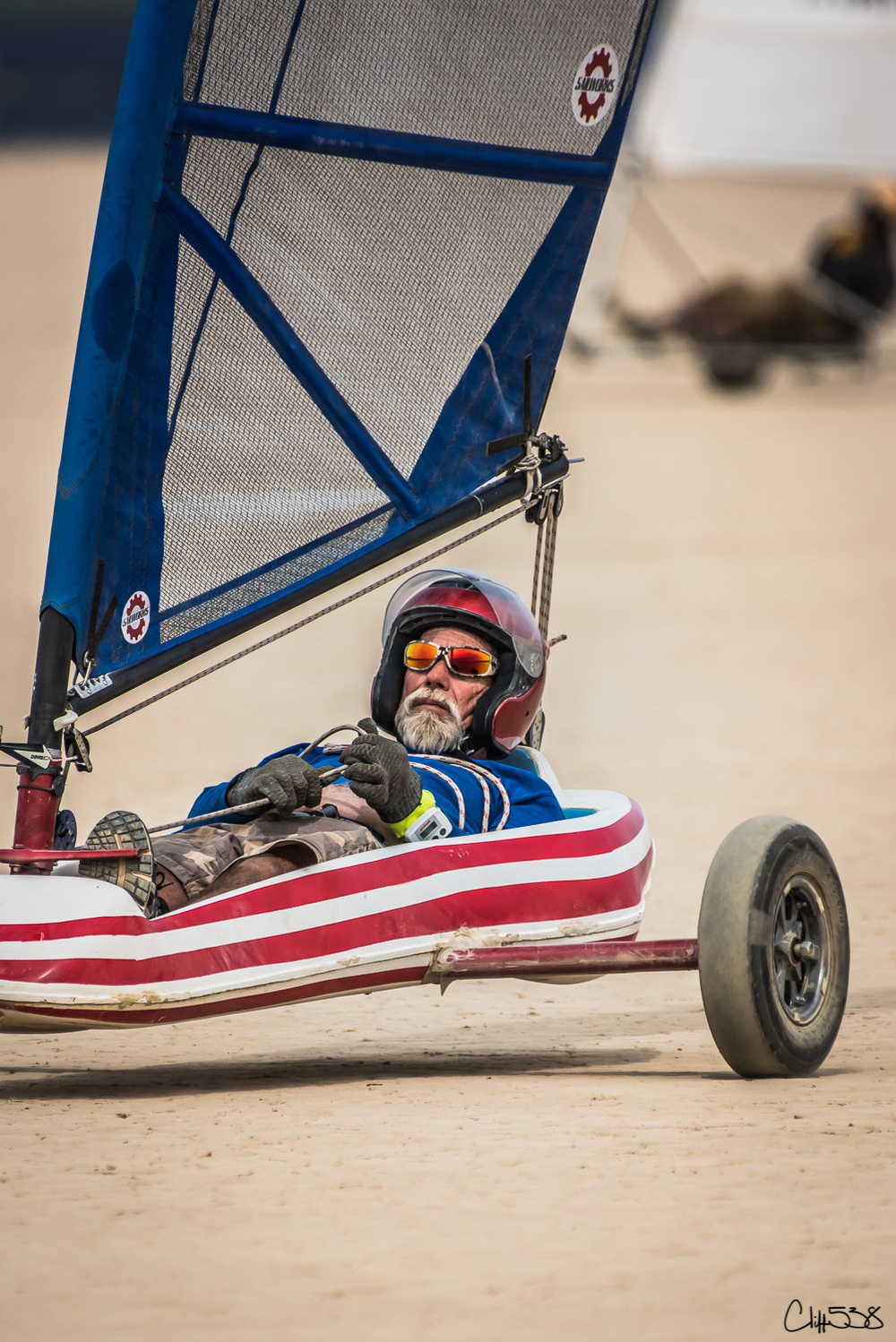 A person is riding a land sail, a small vehicle with a sail, on a sandy surface while wearing protective gear.