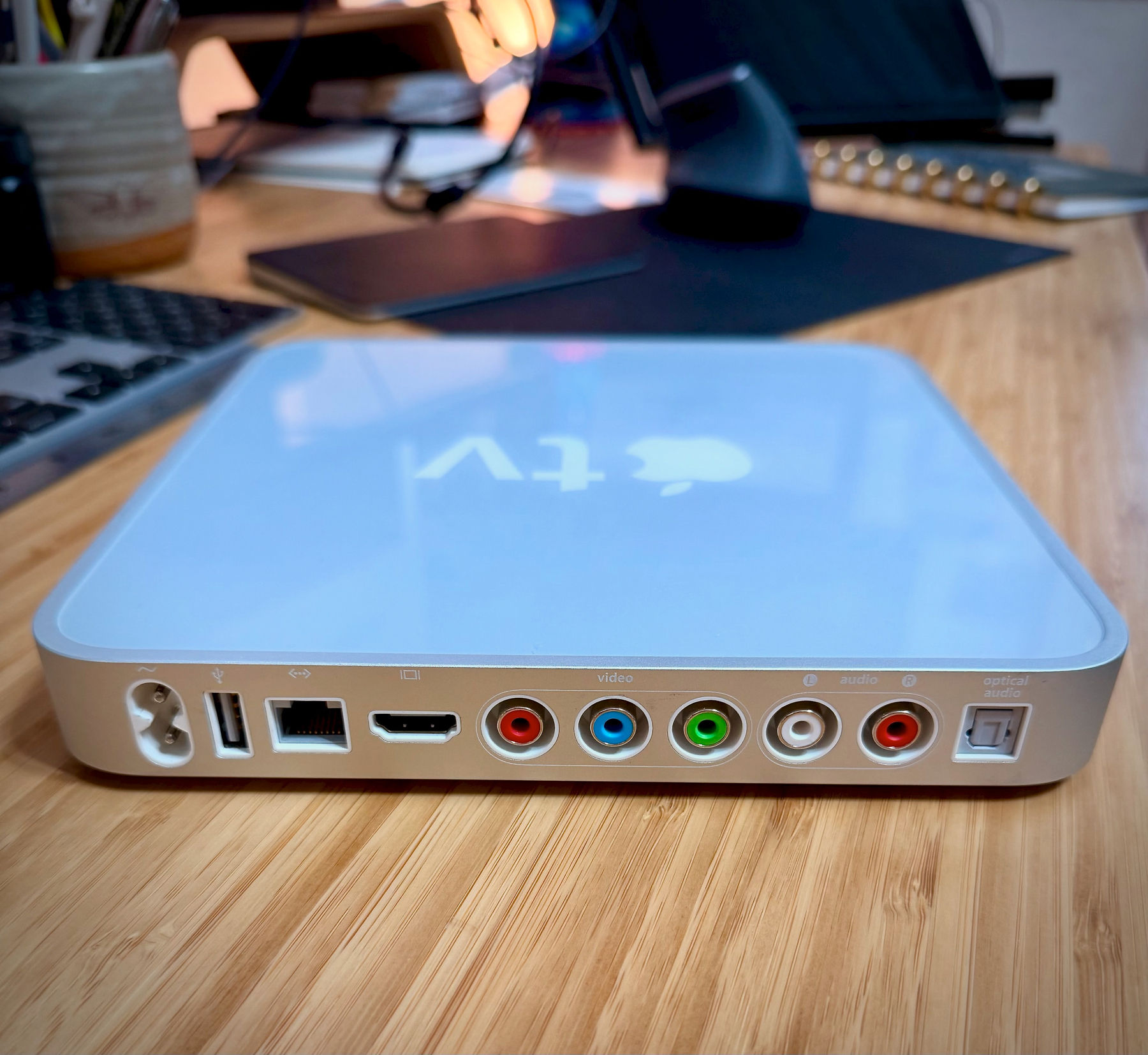 A digital media player with multiple ports is placed on a wooden desk surrounded by various electronic accessories.