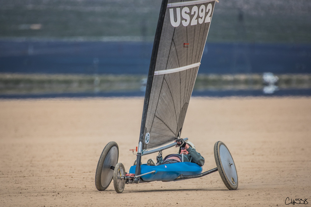 A person is sailing a land yacht with a large sail on a sandy surface.