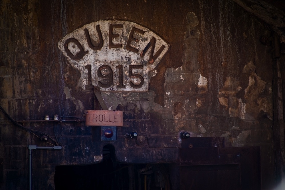 An old, weathered wall features a sign reading QUEEN 1915 and a smaller handwritten sign says TROLL.