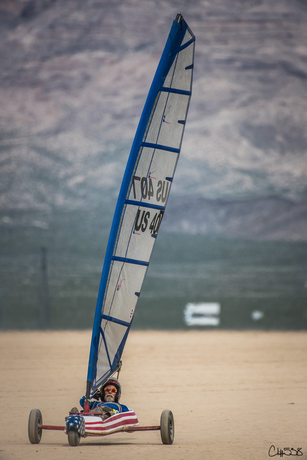 A person is driving a land yacht with a large sail on a desert landscape.