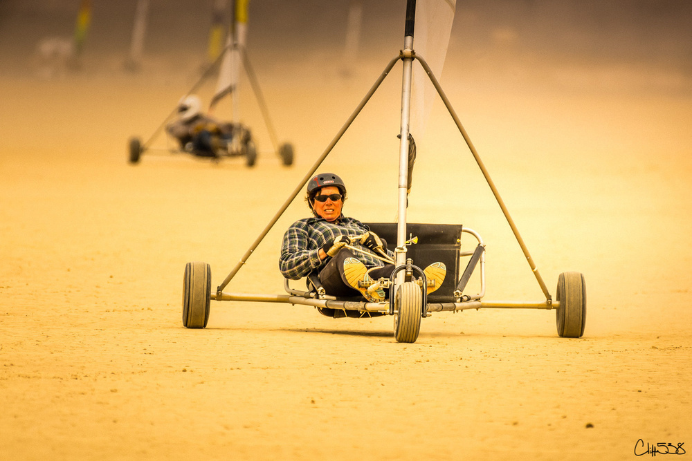 A person wearing a helmet is driving a land sail cart on a sandy surface with another cart in the background.