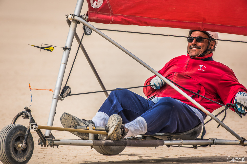 A person is enjoying a ride in a wind-powered land yacht on a sandy surface.