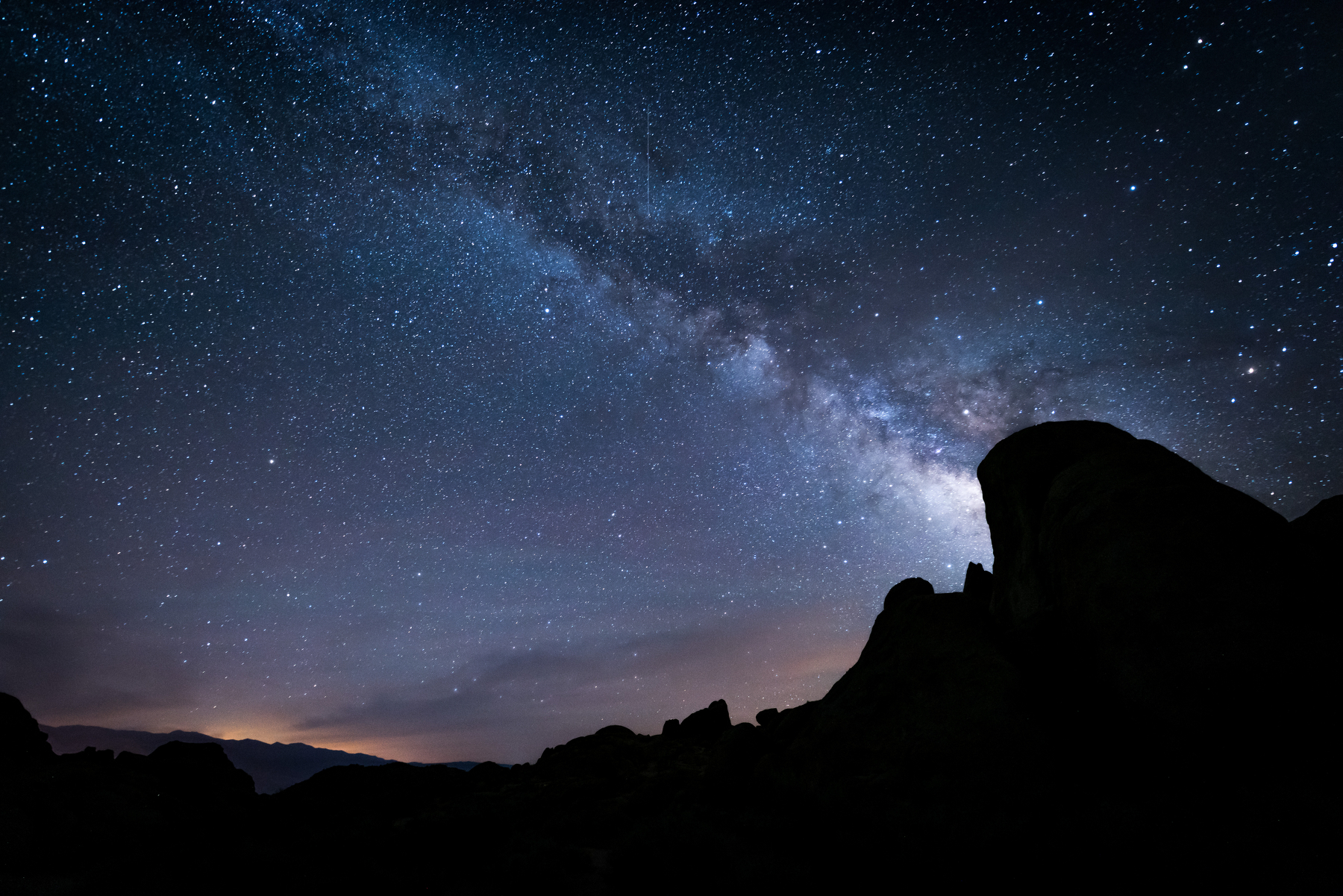 Auto-generated description: A stunning night sky filled with stars and the Milky Way stretches above silhouetted rocky formations.