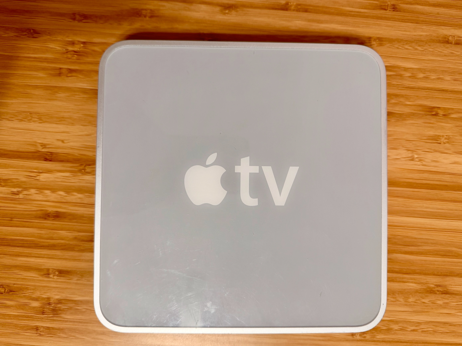 A square-shaped Apple TV device is placed on a wooden surface.