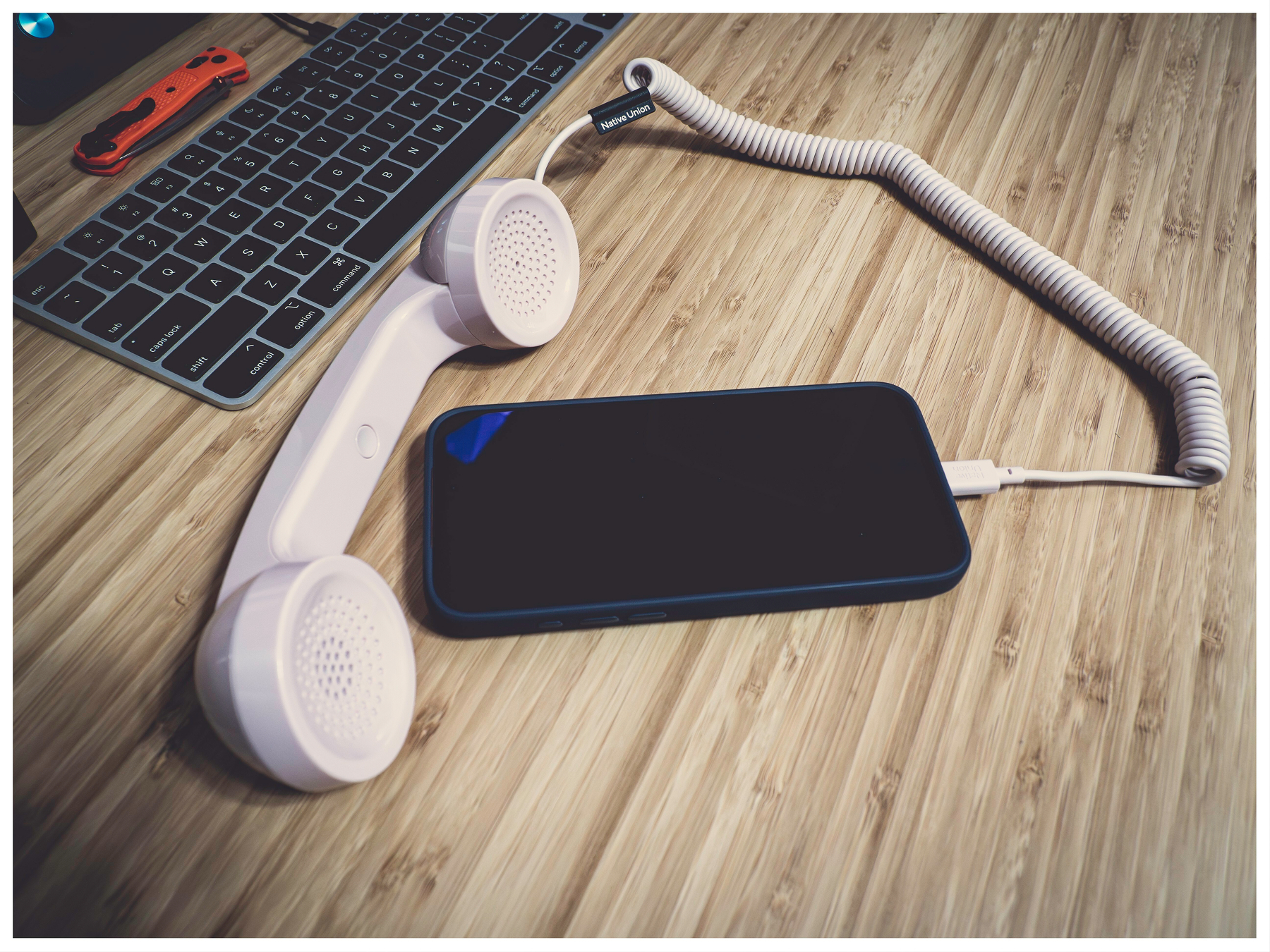picture of an old phone handset plugged into an iPhone, sitting on an office desk.